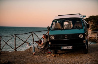 Blauer VW T3 Bulli mit Freunden und Gitarre im Sonnenuntergang am Mittelmeer